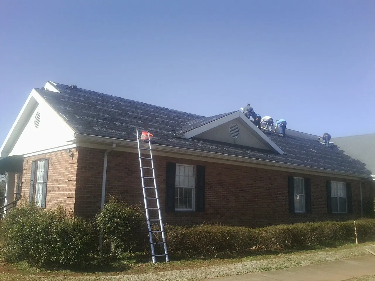 Crew tearing shingles off a brick ranch roof with a ladder set — Emergency Roof Repair work by our crew in North Dartmouth