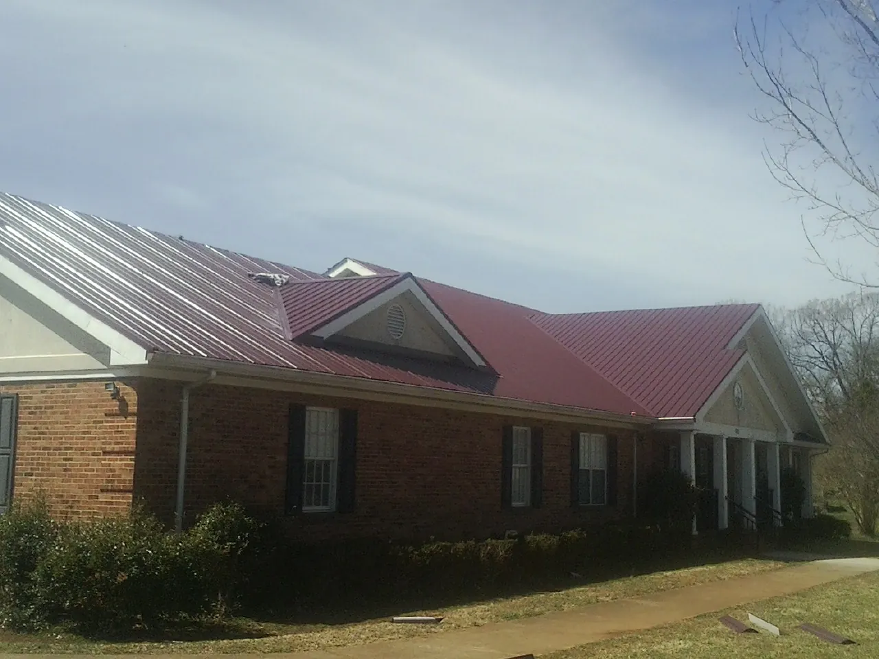 Red metal roof with gabled entries on a long brick building, from a Hail Damage Roof Repair job in North Dartmouth