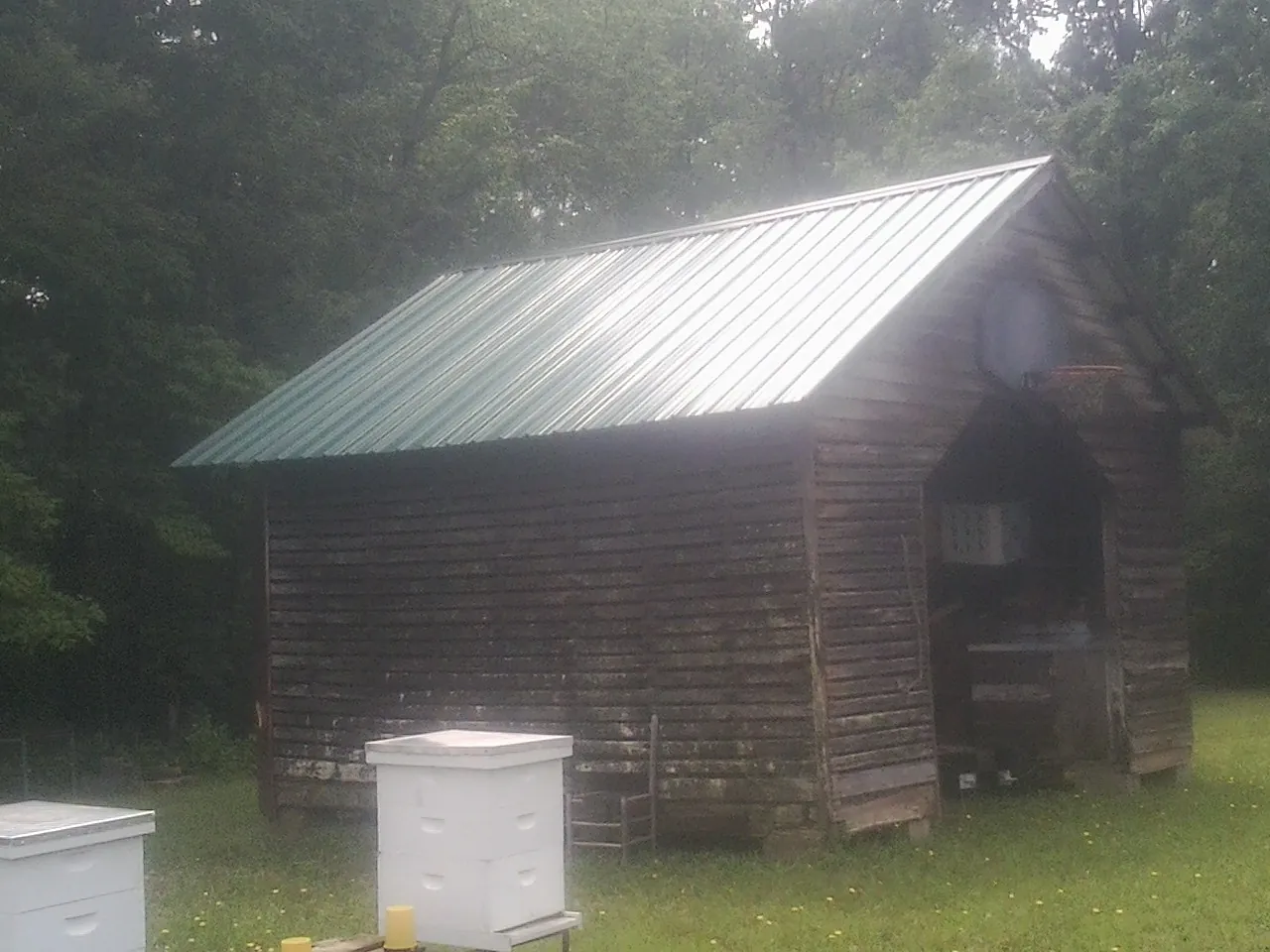 Green metal roof on a weathered barn beside stacked beehives in North Dartmouth
