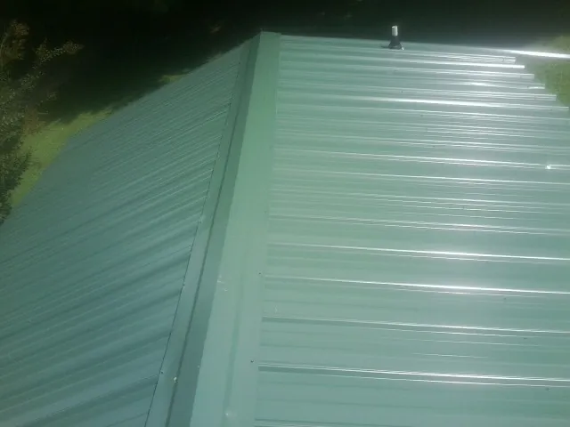 New green metal panels meeting at the ridge of a roof — Flat Roof Repair work by our crew in North Dartmouth