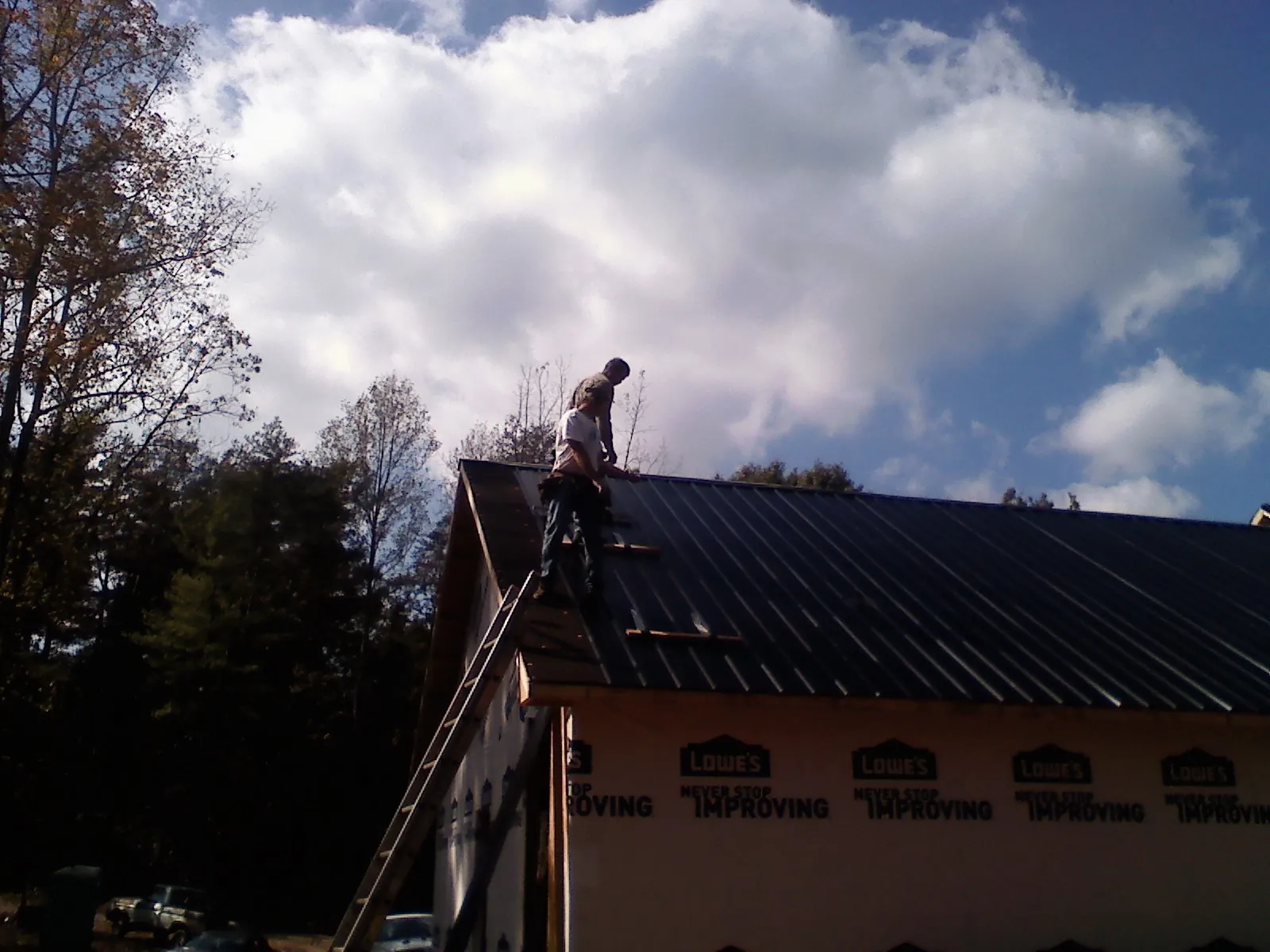 Roofer fastening dark metal panels high against a cloudy sky, from a Roof Inspection job in North Dartmouth