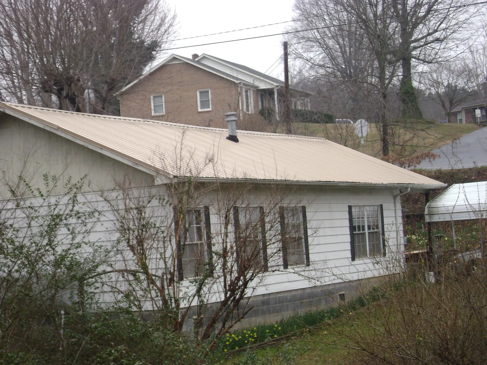 Tan metal roof on a white sided house set into a hillside — Commercial Roofing by Roofing Brothers in North Dartmouth