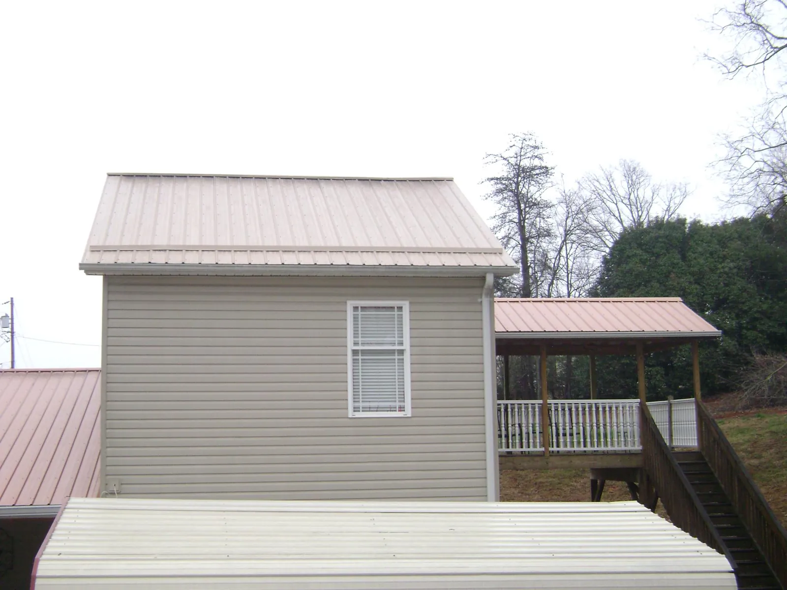 Tan metal roofs on a two story addition and attached porch, from a Roof Replacement job in North Dartmouth